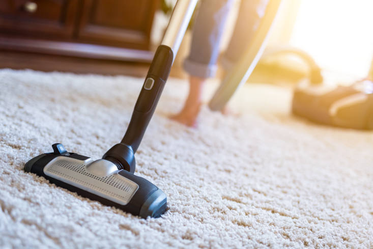 Young woman using a vacuum cleaner while cleaning carpet in a house.